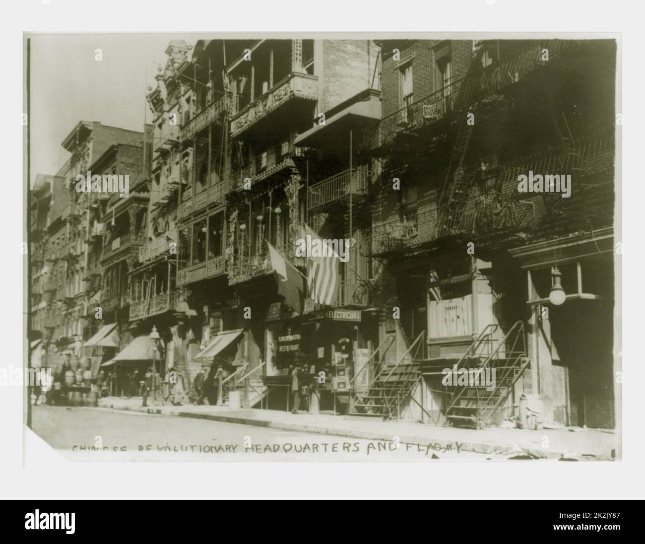U.S. and Chinese flags hanging from Chinese revolutionary headquarters in New York city 1911. Photo shows the Young China Association headquarters on the second floor of 12 Mott Street in New York City, flying the flag of the Chinese revolutionary movement. The headquarters are above the Boston Cigar store, to the right of the Flowery Kingdom Restaurant and to the left of Morning Star Mission facilities. Stock Photo