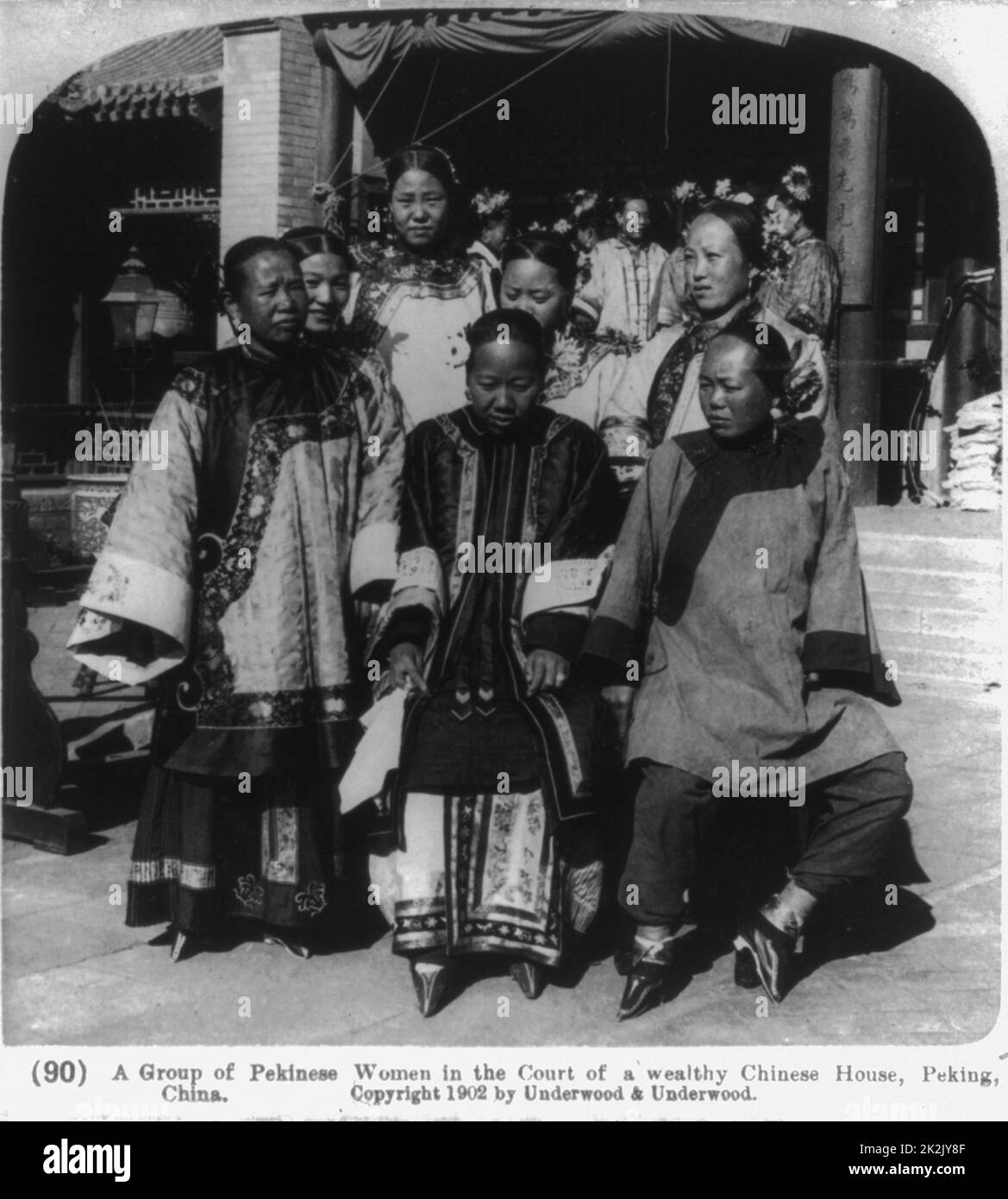 A group of Pekinese women in the court of a wealthy Chinese house, Peking, China c1902. photographic print on stereo card or stereograph. note the men in rows holding swords. Stock Photo