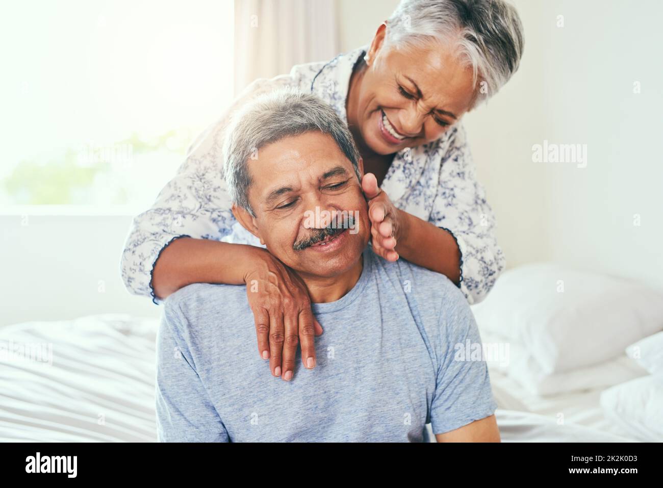 Wow Im getting spoiled today. Shot of a cheerful mature couple holding each other while being seated on a bed at home during the day. Stock Photo