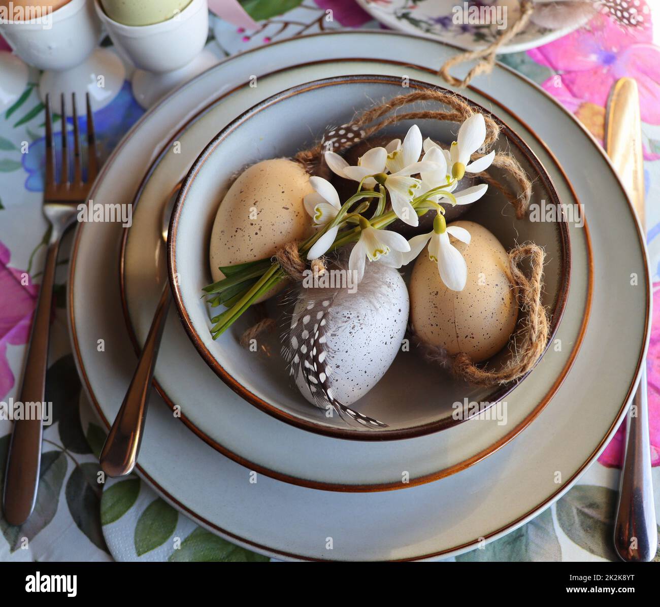 Stylish Easter table setting with egg in bowl on table. Modern natural dyed easter egg, flowers on plate and cutlery. Easter festive table decorations Stock Photo