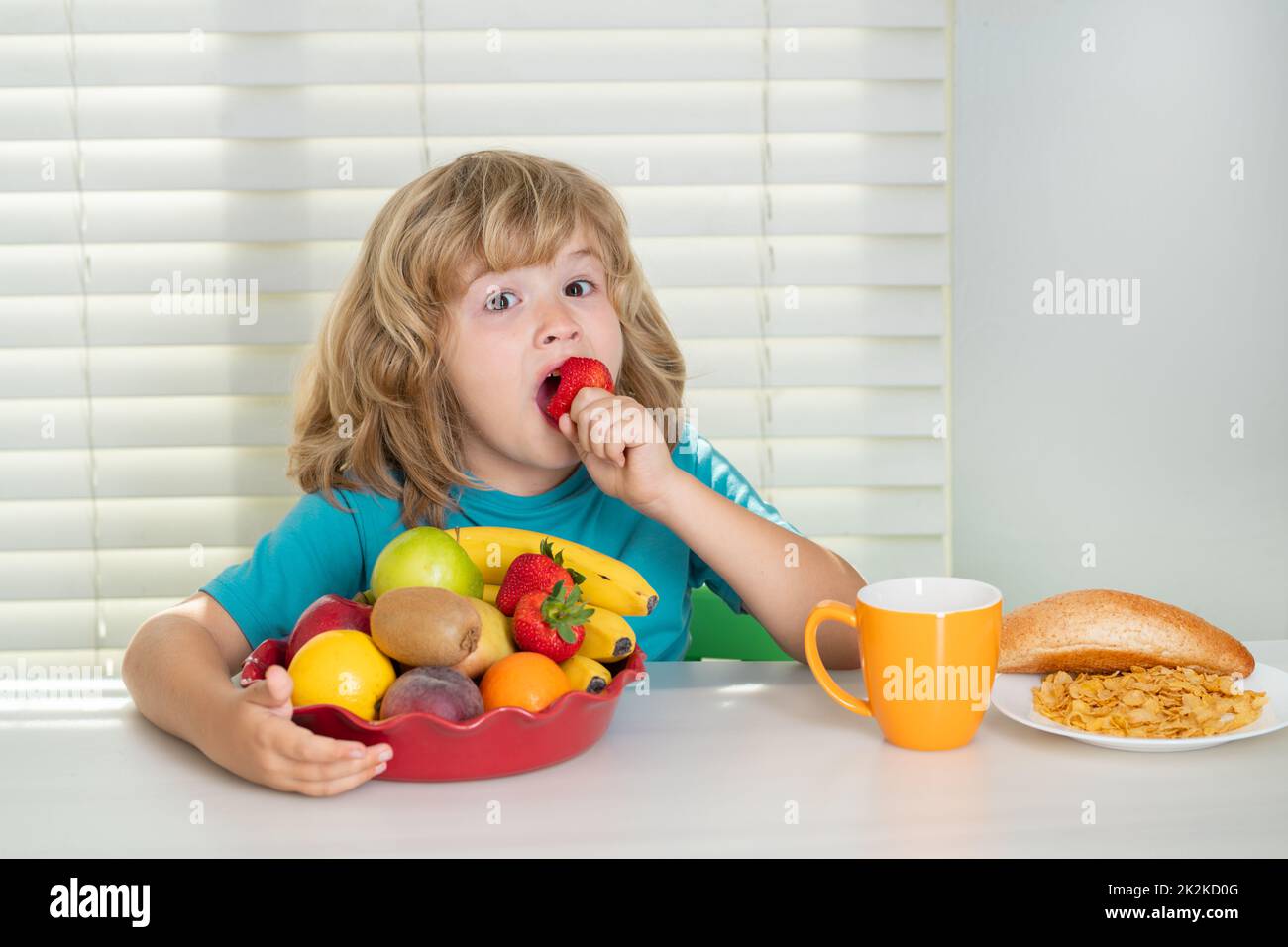 Child with strawberry, summer fruits. Child in the kitchen at the table eating vegetable and fruits during the dinner lunch. Healthy food, vegetable Stock Photo