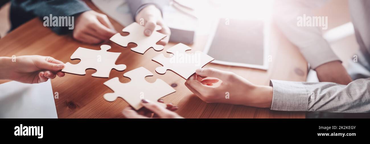Buisnesswomen and buisnessmen working together while putting together puzzles. Stock Photo