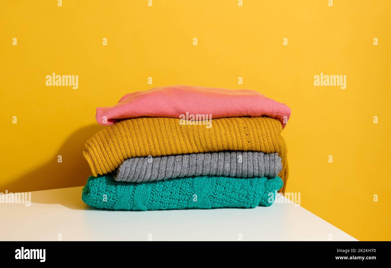 stack of folded knitted sweaters on yellow background. Comfortable clothes, wash Stock Photo