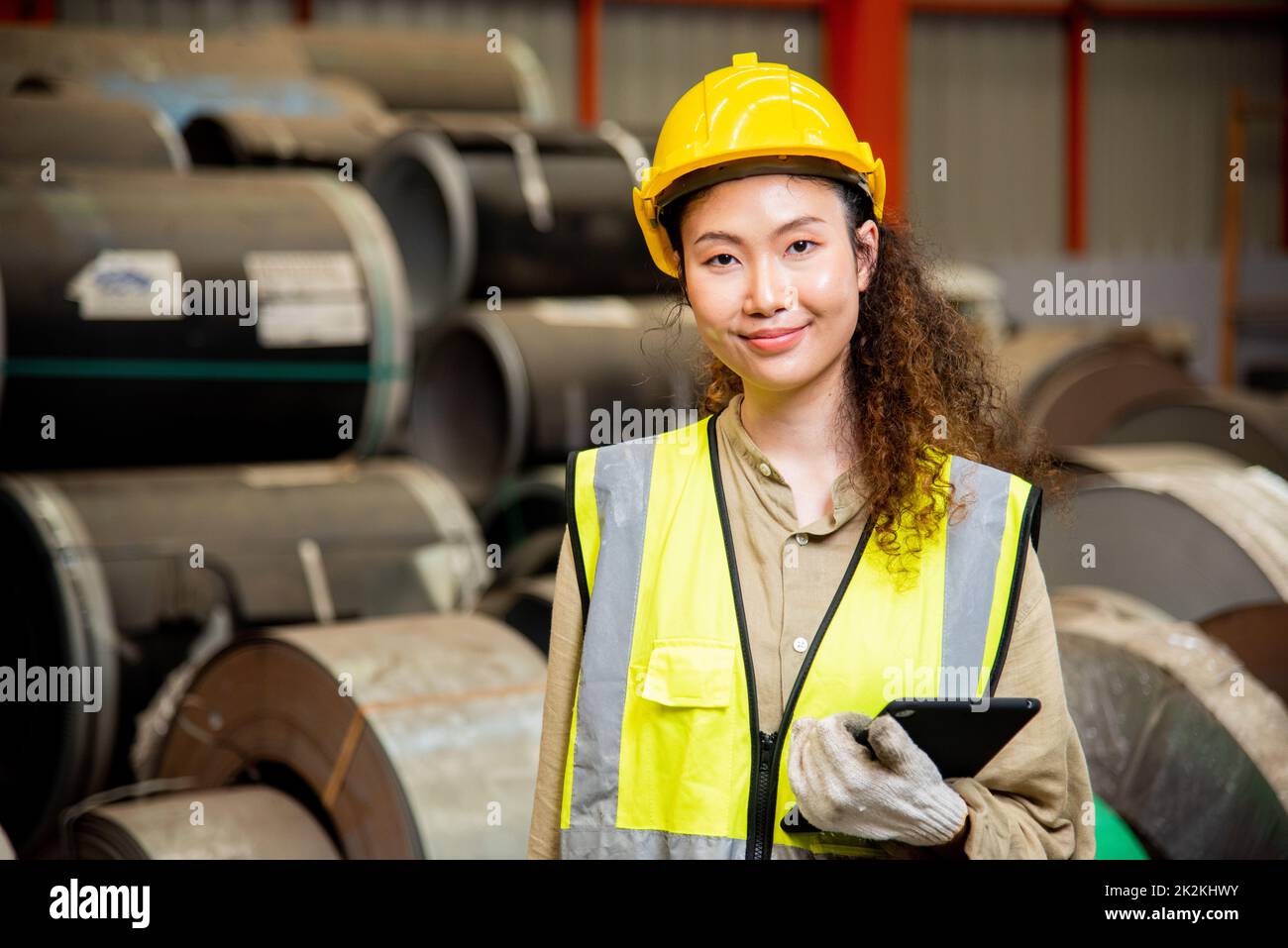 Asian worker woman with safety vest holding tablet computer walking to checking warehouse storage in factory Stock Photo