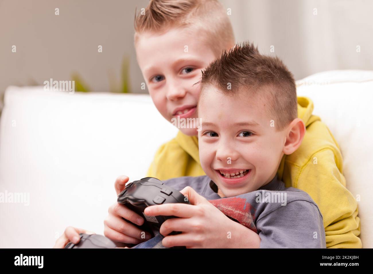 Two young brothers playing video games together on a sofa Stock Photo