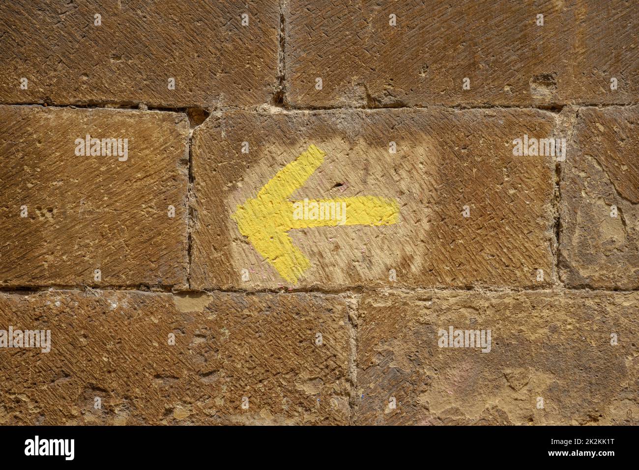 Yellow arrow painted on a stone wall indicates the direction of the pilgrimage to Santiago de Compostela Stock Photo