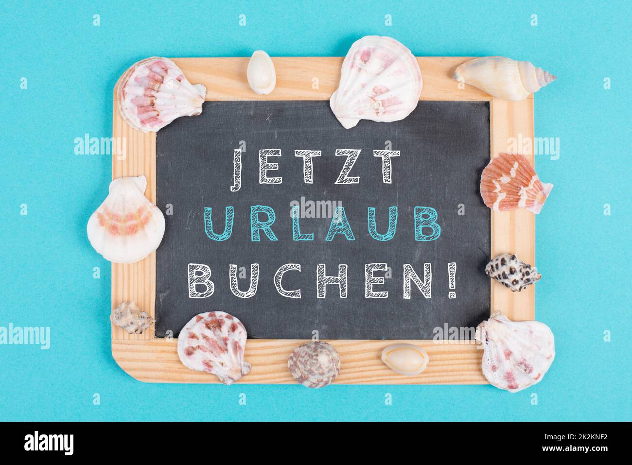 Book vacation now is standing in german language on the chalkboard, seashells bulit frame, holiday and summertime topic, travel concept Stock Photo