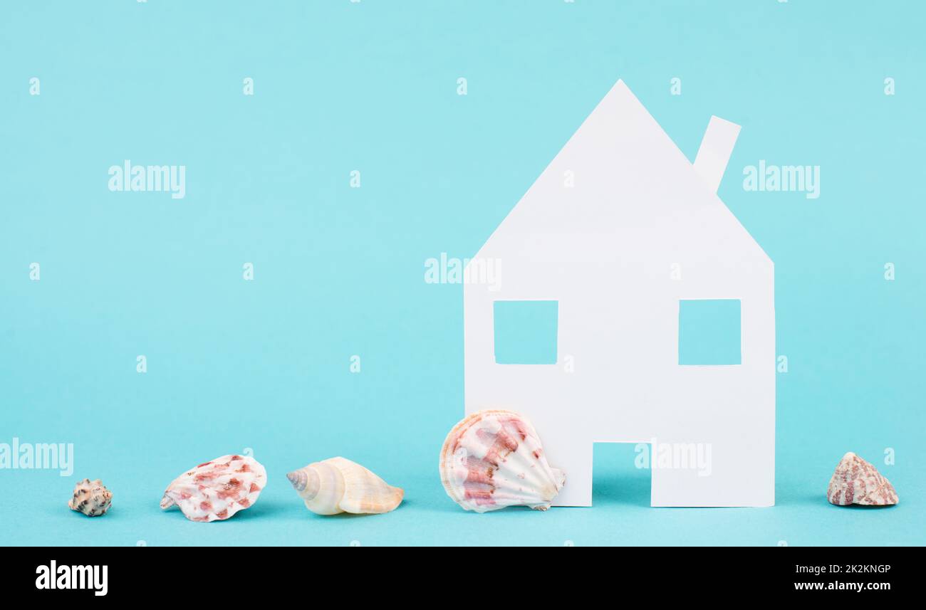 White house on a blue colored background with sea shells, booking an appartment, hotel or lounge for vacation, holidays in summer on the beach, copy space for text Stock Photo