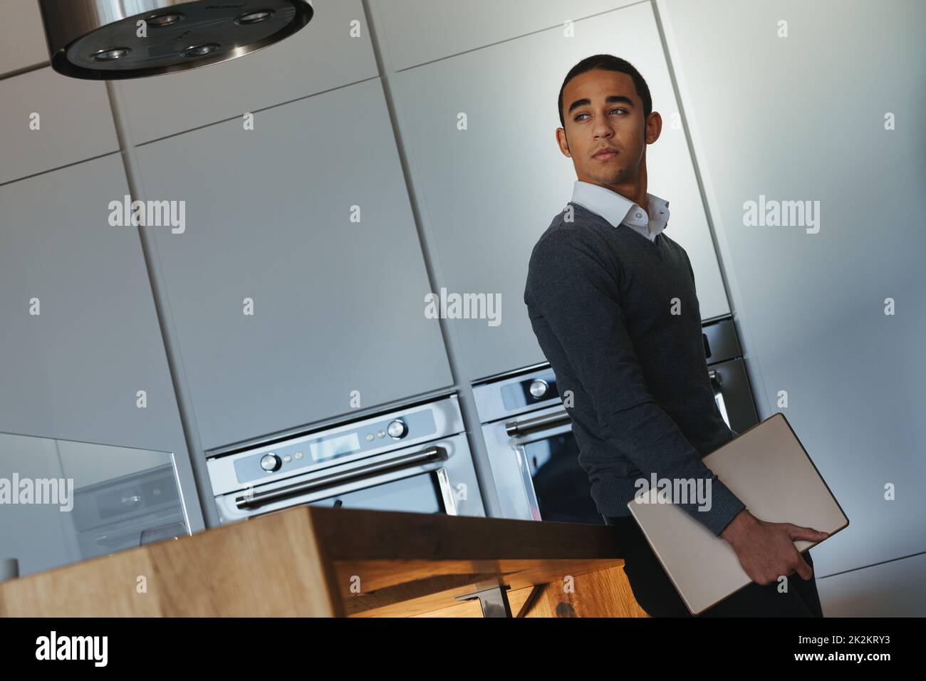 Black man standing in a modern fitted kitchen holding a laptop Stock Photo