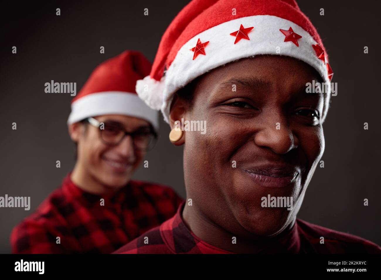 Charismatic male friends grinning at the camera in Santa Hats Stock Photo