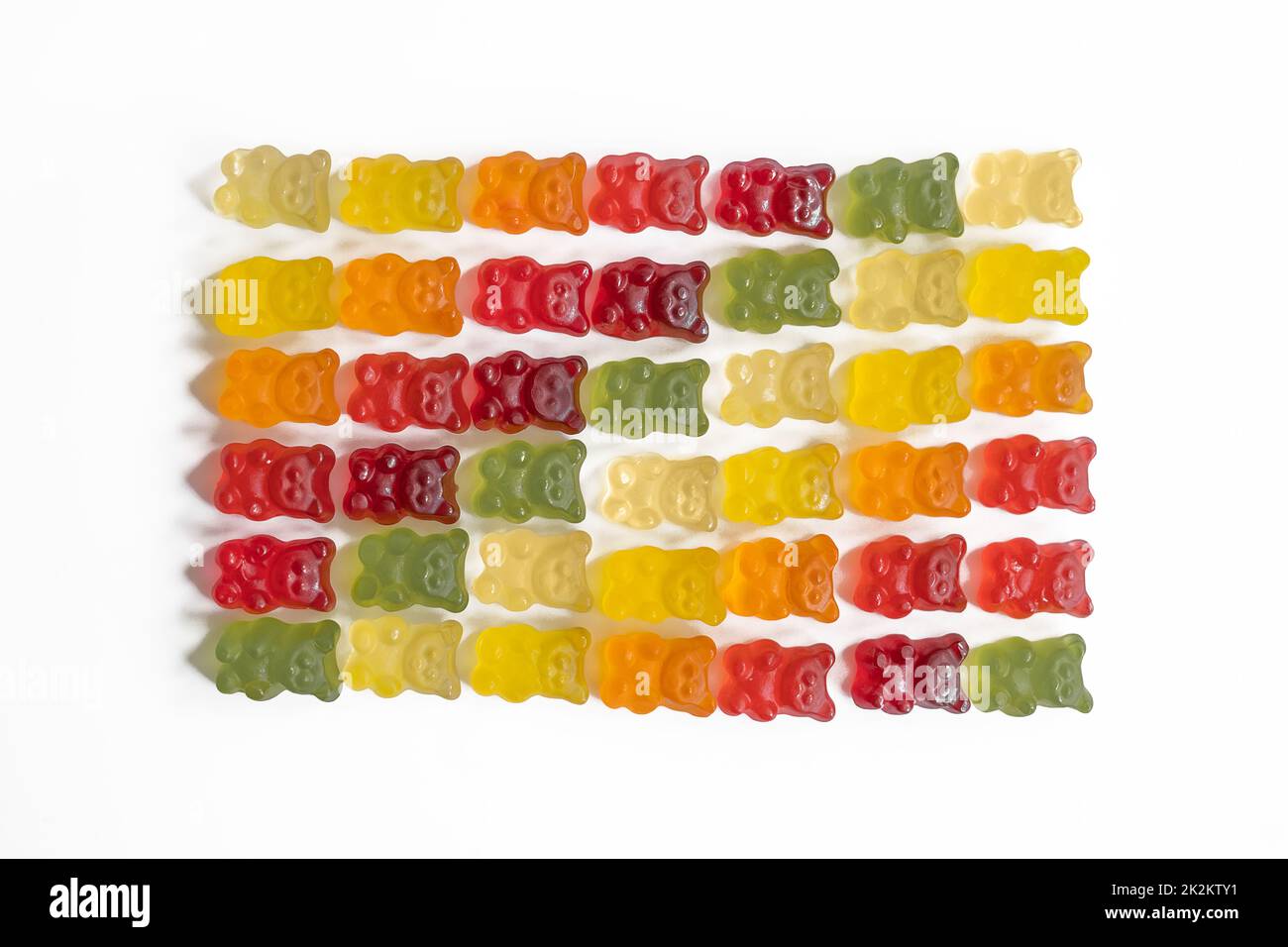 top view of multi-colored gummy bears arranged in rows by color as a gradient on a light background with negative space close-up Stock Photo