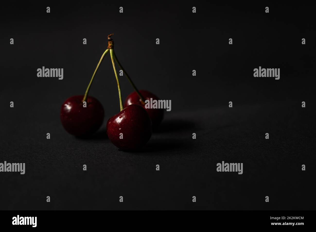 Three cherries are placed on a black background with negative space Stock Photo