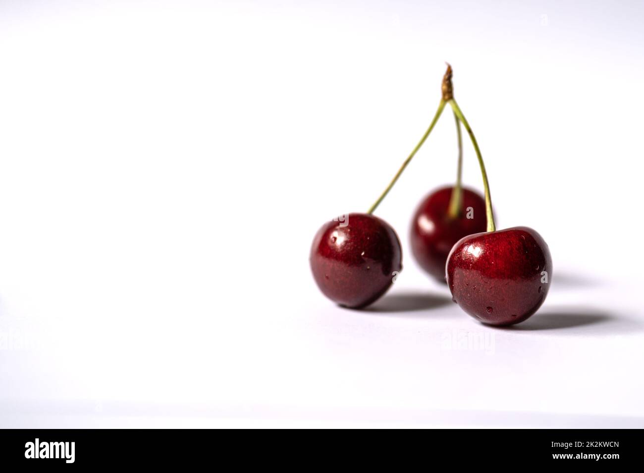 Three cherries are placed on a light background with negative space Stock Photo
