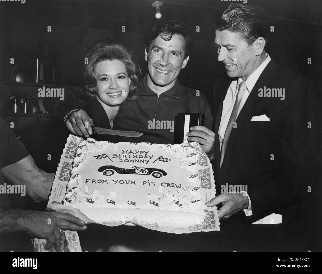 The film crew gives a suprise birthday cake to the director. Angie Dickinson, John Cassavetes and Ronald Reagan around the cake. Film: The Killers, USA, 1964 Stock Photo