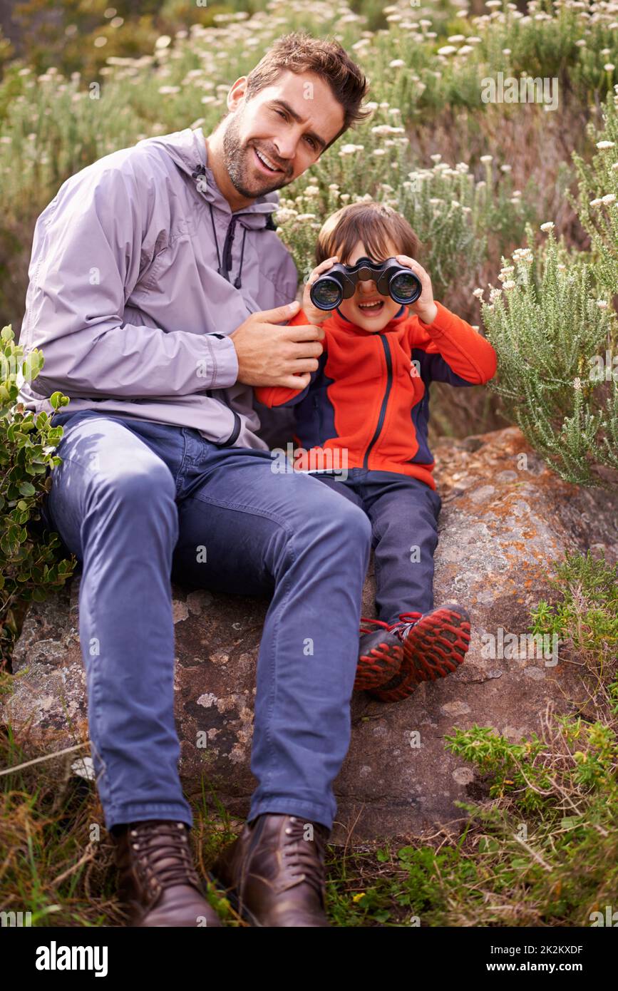 We see you. a little boy looking through binoculars while on a hike with his father. Stock Photo