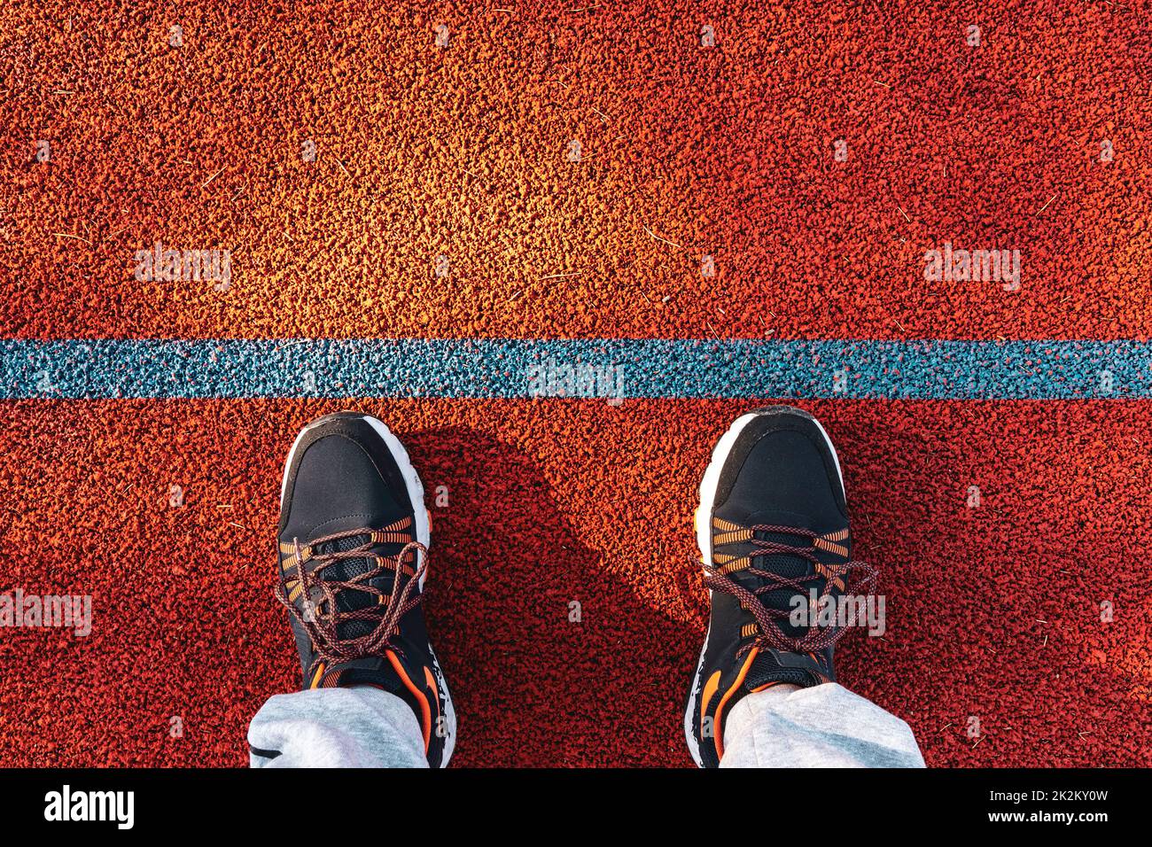 Feet in sneakers stand on the running track with blue line Stock Photo