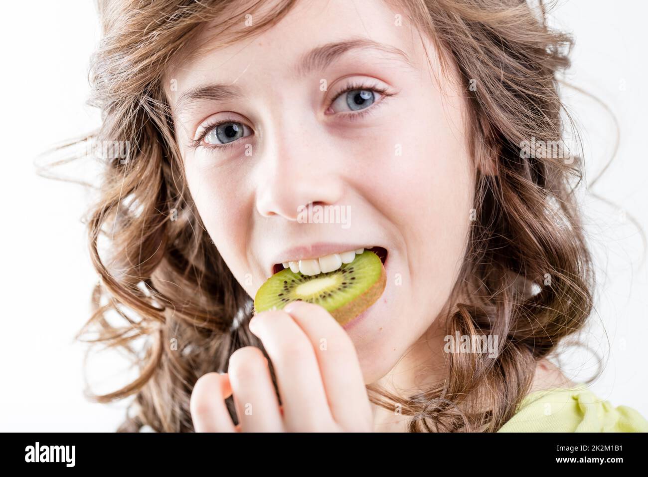 close up portrait of a girl putting a kiwi slice in her mouth she's
