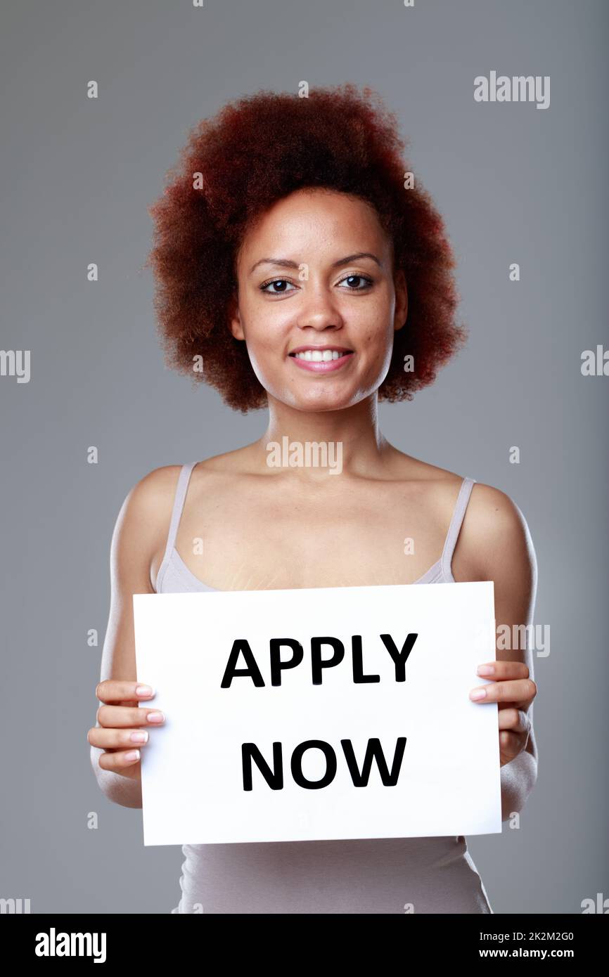 Happy friendly young Black woman holding sign Apply Now Stock Photo