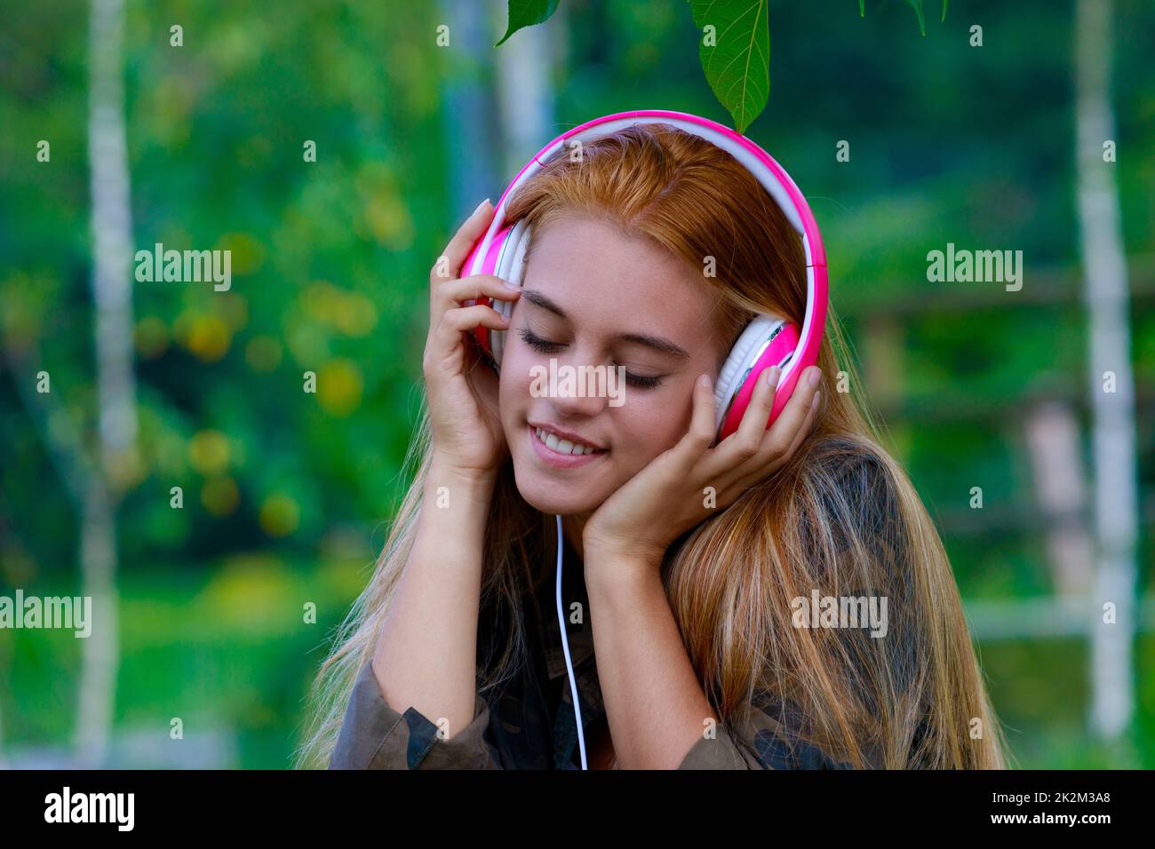 girl with pink headphones listens to music in the park Stock Photo