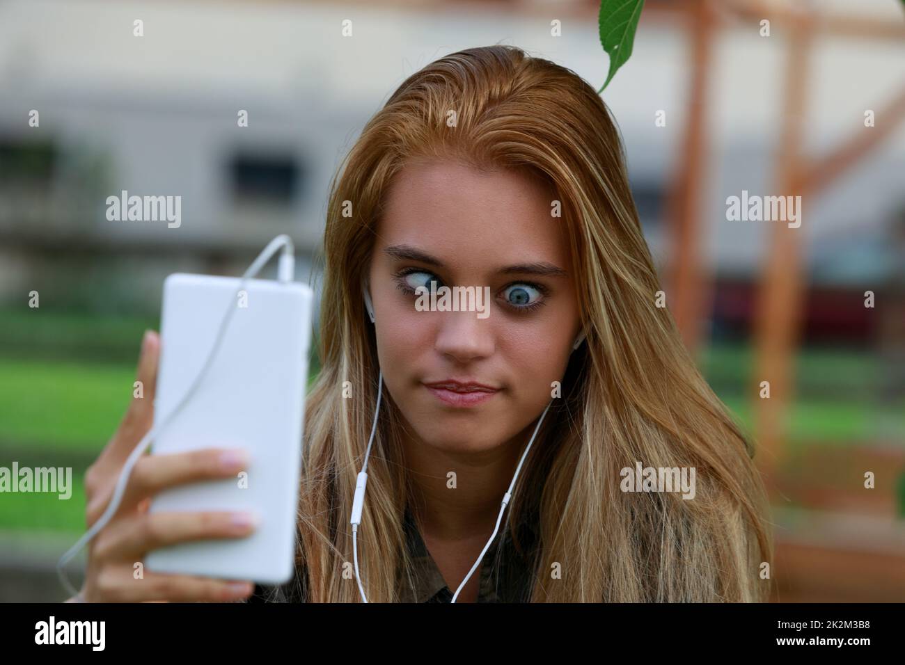 girl makes funny faces and crooked eyes using her mobile phone Stock