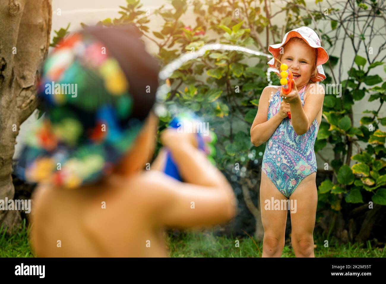 little girl and boy playing with water guns at garden on hot summer day. children having fun outdoors Stock Photo