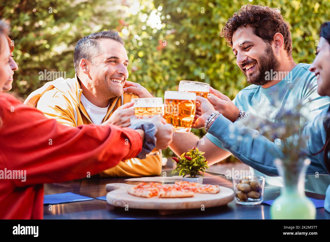 Cheerful group of young friends toasting beer glasses and having fun outdoors - People having lunch in the garden restaurant - millennials habits, peo Stock Photo