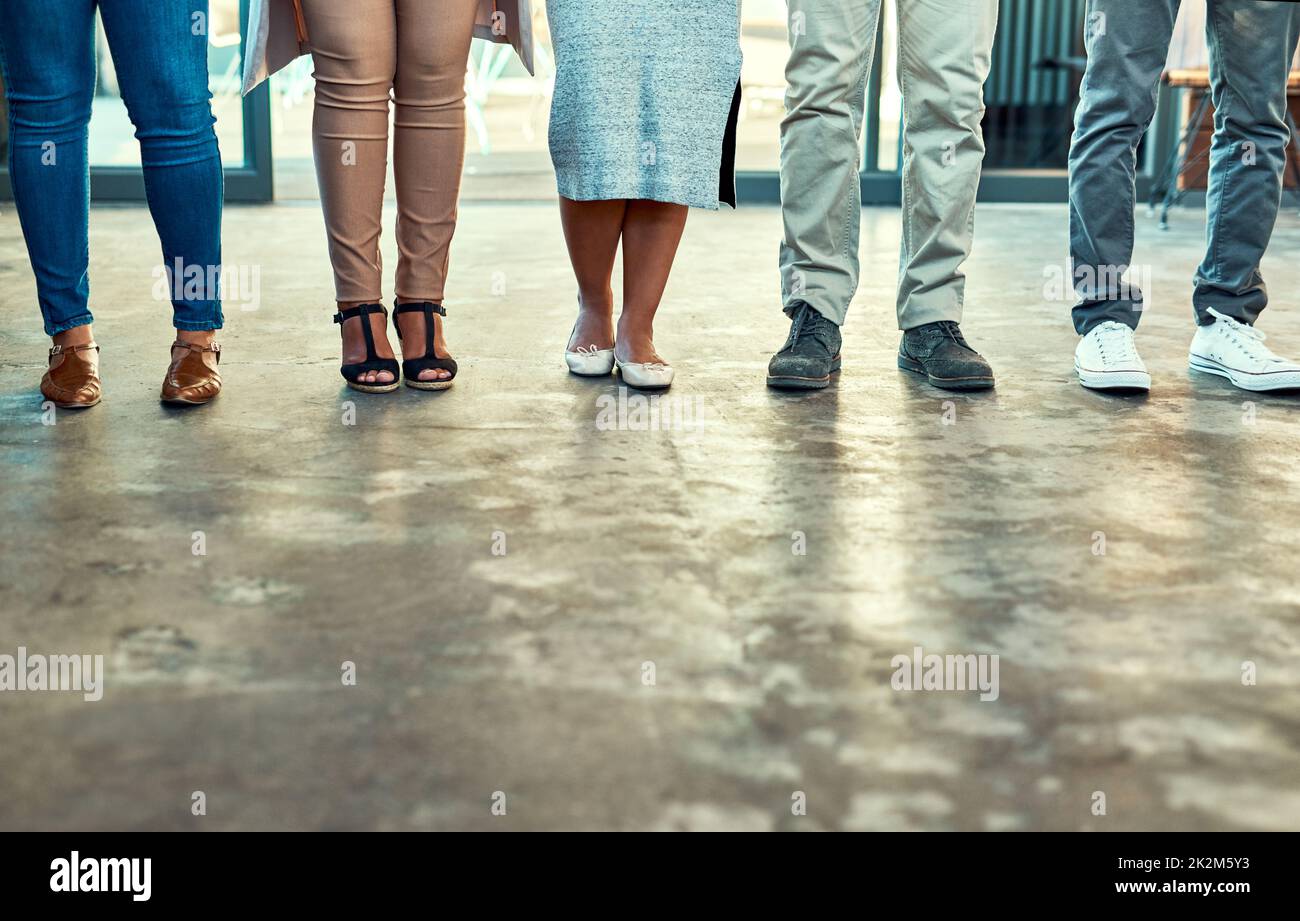 Theres no issue when you have nice shoes. Low angle shot of a group of unrecognizable work colleagues standing side by side in a straight line inside the office during the day. Stock Photo