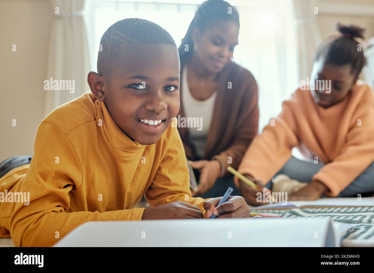 I love not having to go to school. Shot of a young boy completing his homework while his mom helps him and his sister. Stock Photo