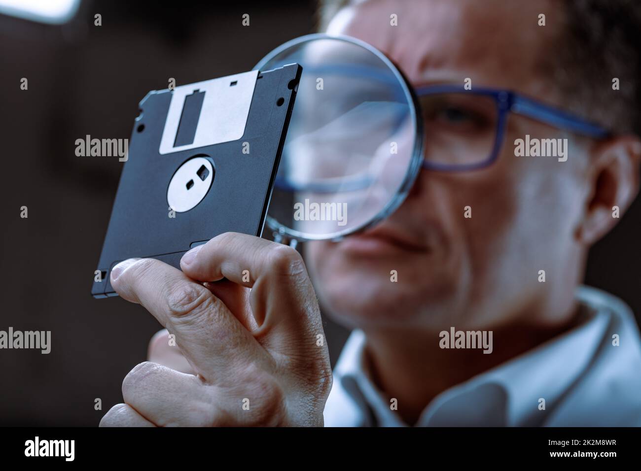 Middle-aged forensics expert examining a retro floppy disc Stock Photo