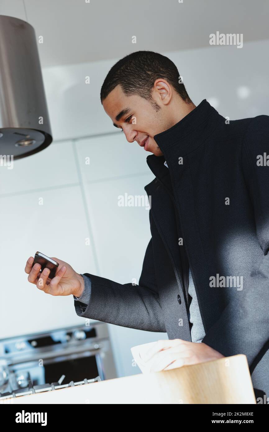Black man preparing a meal reading a message on his smartphone Stock Photo