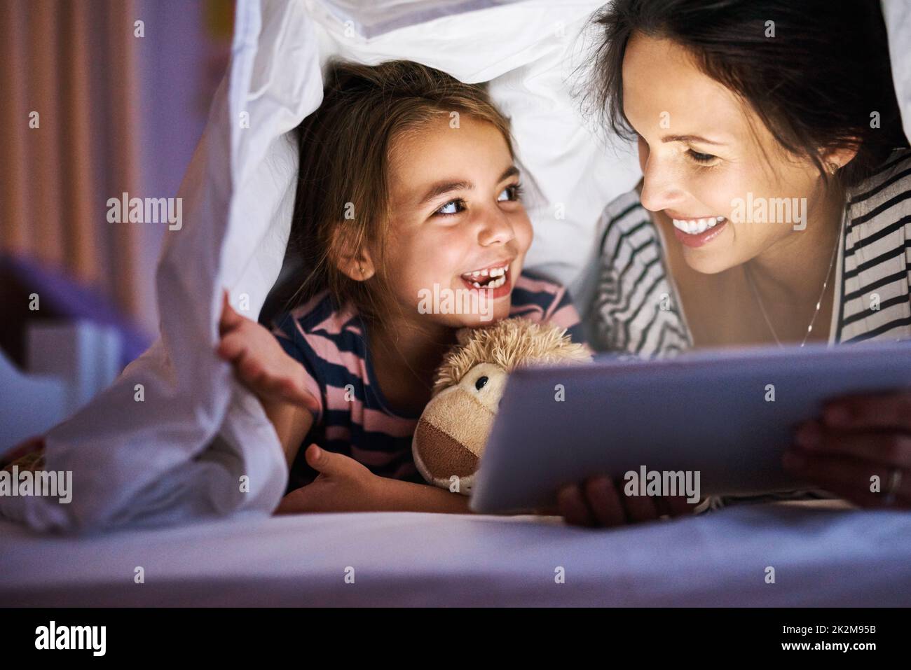 Let me read the next one. Cropped shot of an attractive young pregnant woman reading her daughter a bedtime story on a tablet. Stock Photo