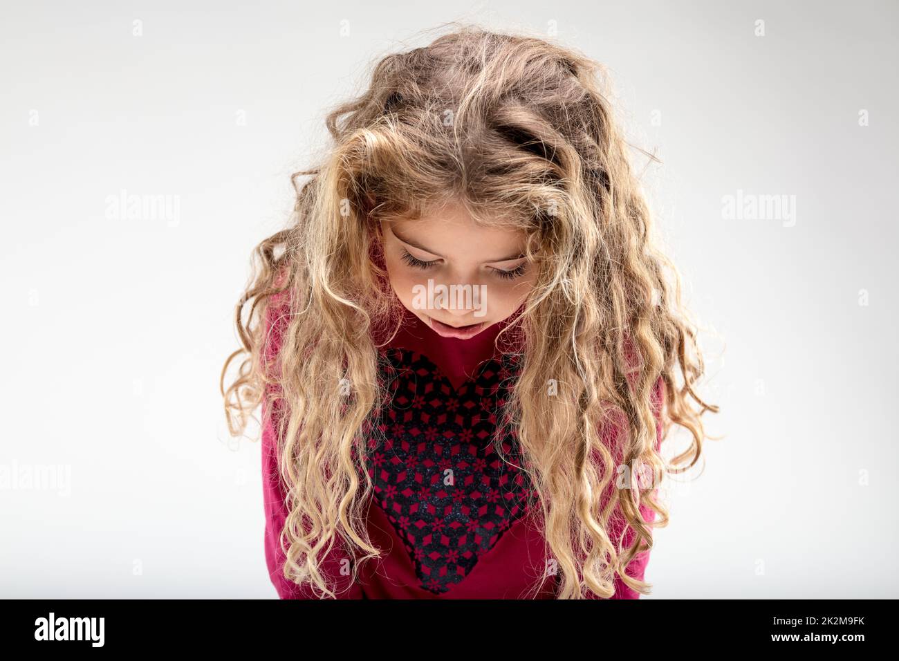 Sad curly-haired schoolgirl with head down Stock Photo