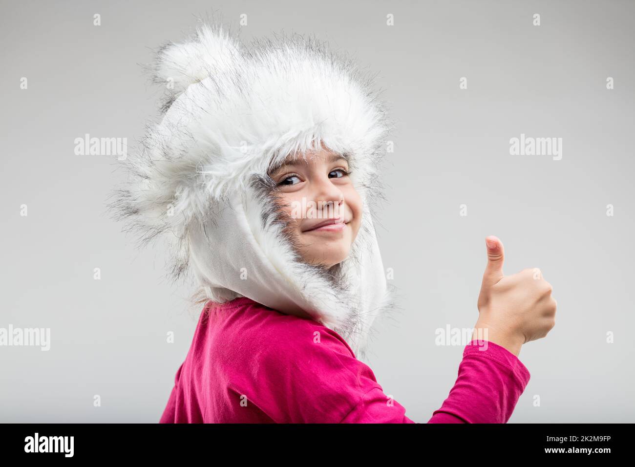 Preteen girl wearing fluffy cap giving thumb up Stock Photo