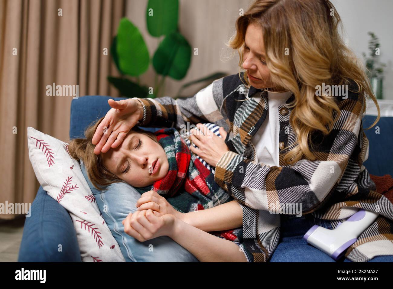 Woman checking temperature with hand of adult ill daughter. Mother