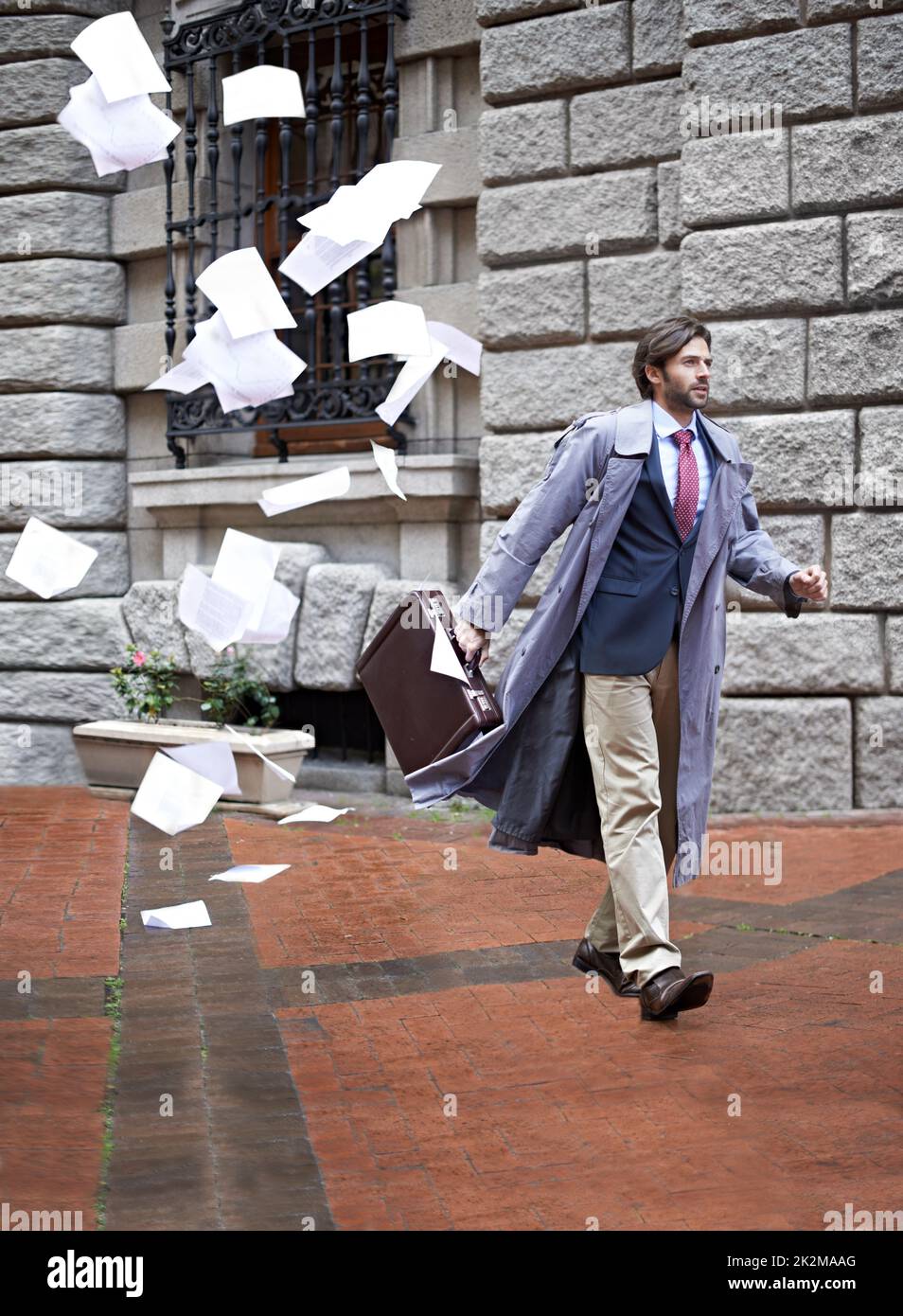 Its not going to be his day.... A businessman unaware that as he walks to work hes losing all his papers. Stock Photo