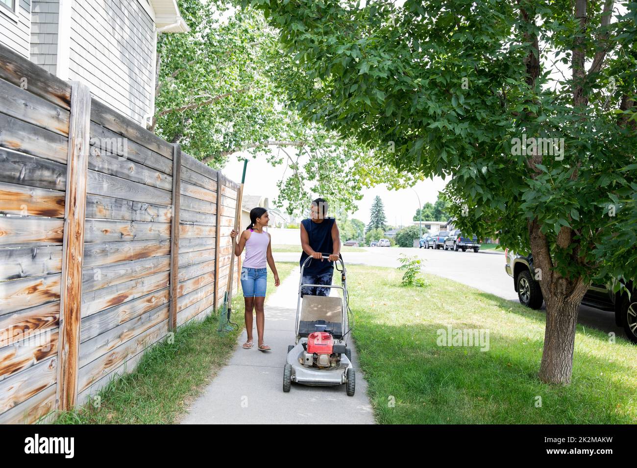 Children walking with lawn mower in neighborhood Stock Photo Alamy