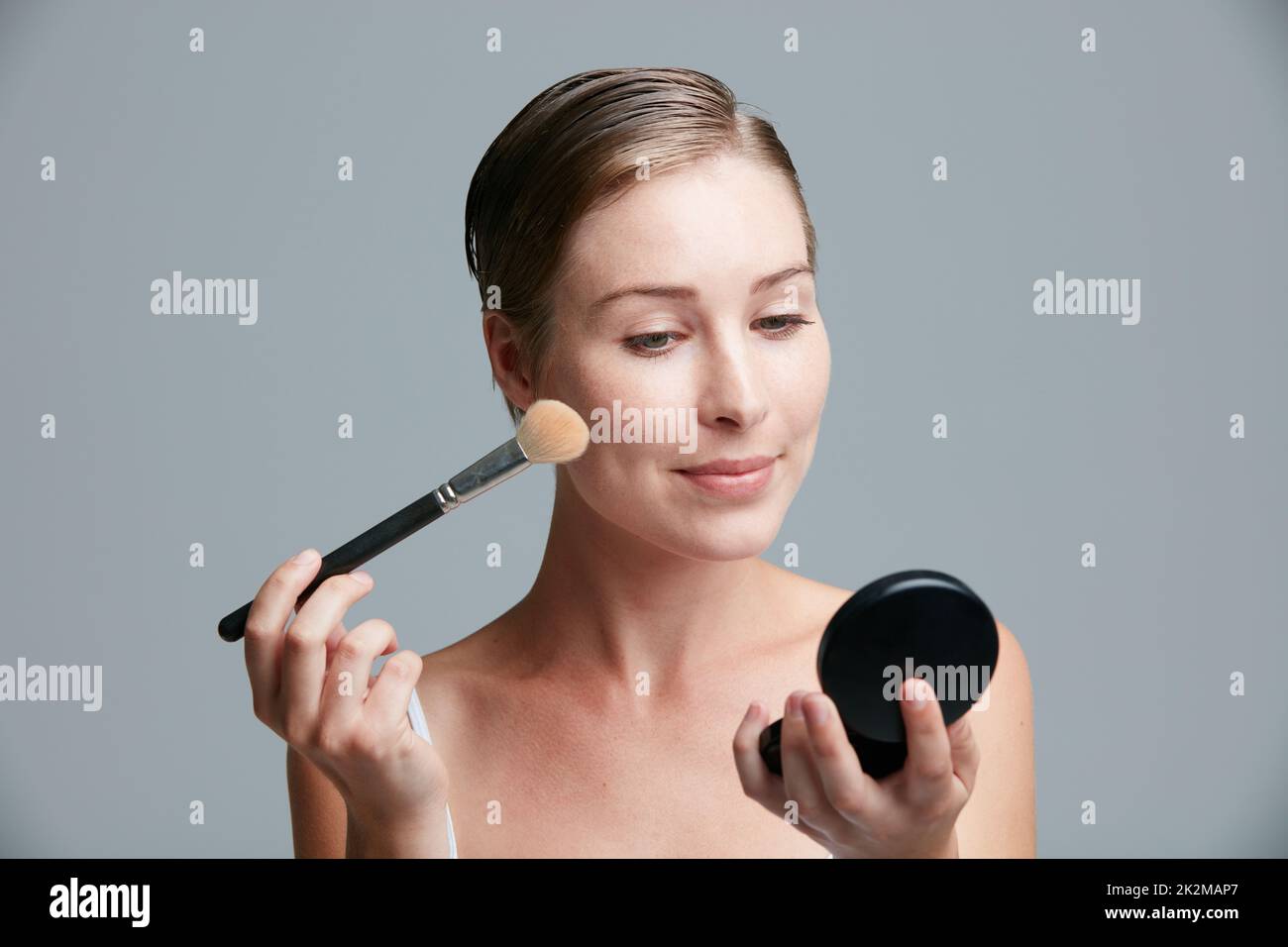 Look your best, let life take care of the rest. Studio shot of an attractive young woman applying makeup with a brush against a gray background. Stock Photo