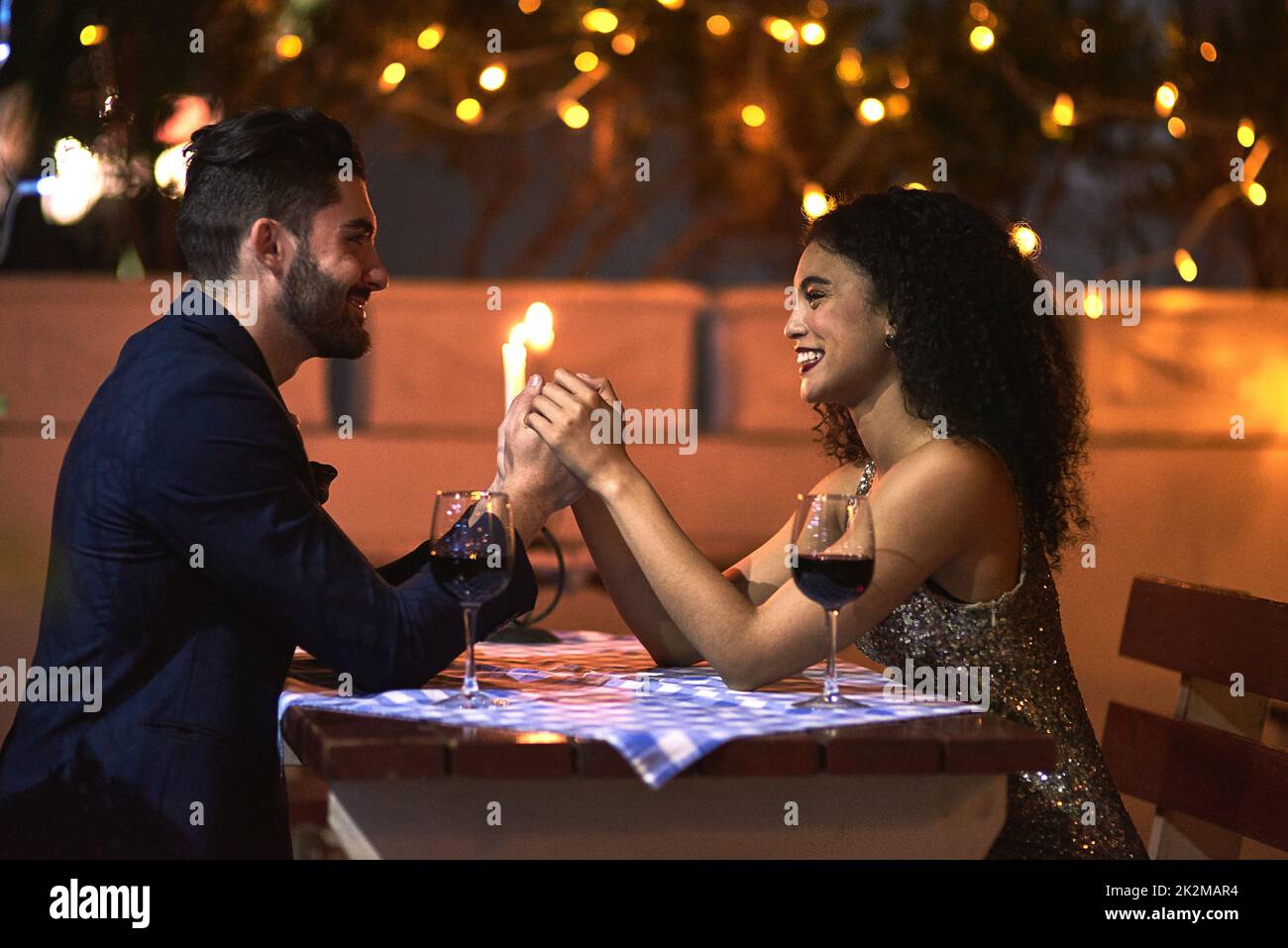 Some quality time with just you and me. Shot of a cheerful young couple holding hands while looking into each others eyes over a candle lit dinner date at night. Stock Photo