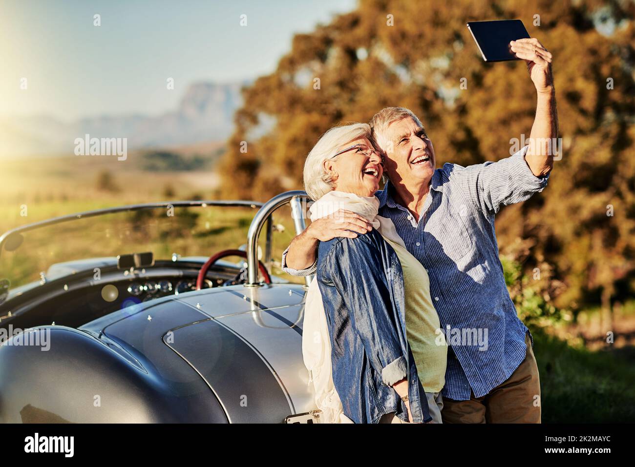 Taking a selfie for the grandkids. Shot of a senior couple posing for a selfie while out on a roadtrip in a convertible. Stock Photo