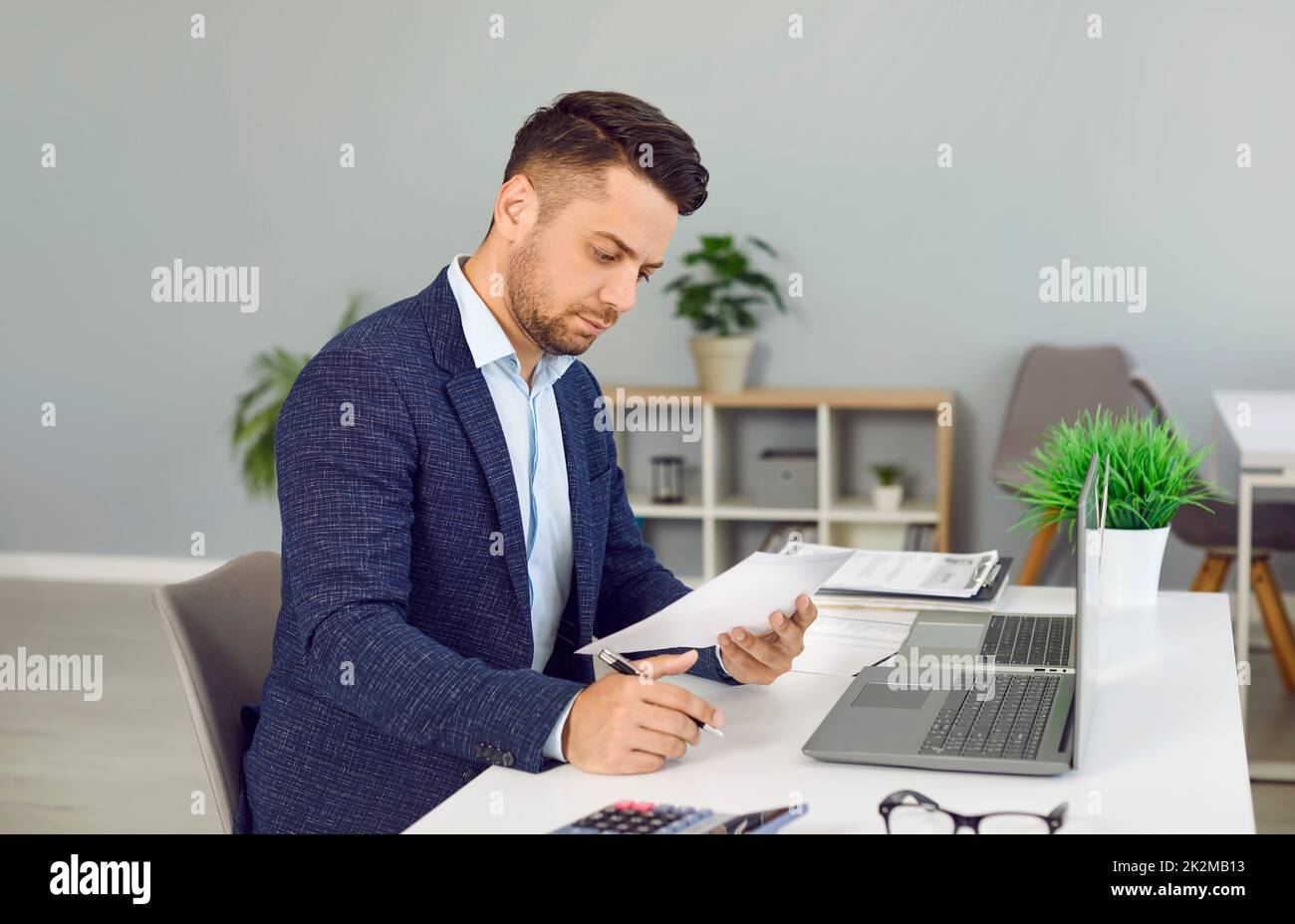 Young man reading some business documents while sitting at his desk in the office Stock Photo