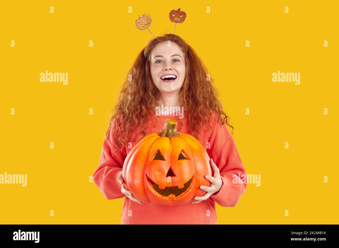 Portrait of cheerful young woman holding Halloween pumpkin with funny carved face on it. Stock Photo