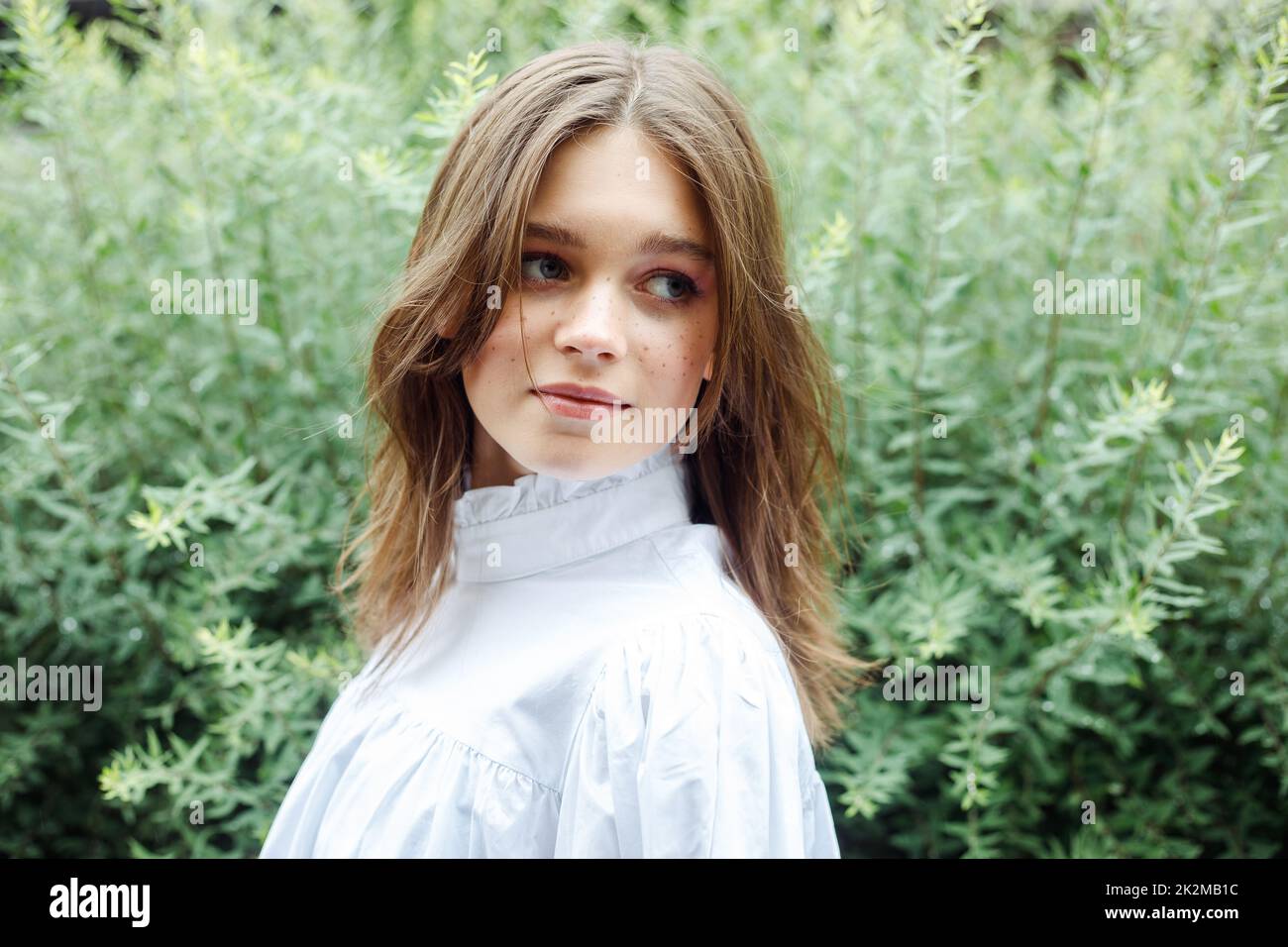 Portrait of lovely young girl in nice white dress standing among ...