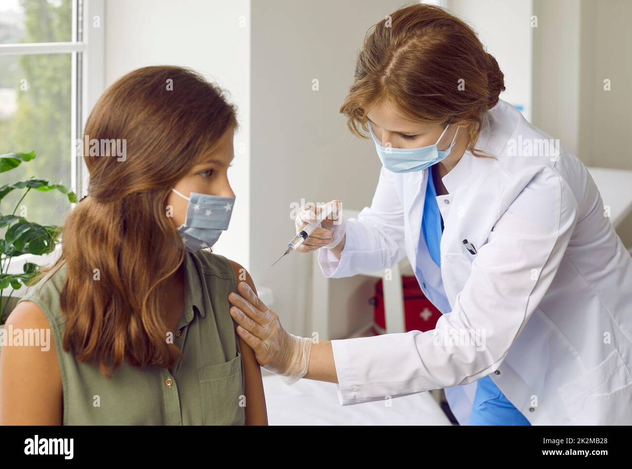 Female nurse or doctor in medical face mask giving vaccine injection to child patient Stock Photo
