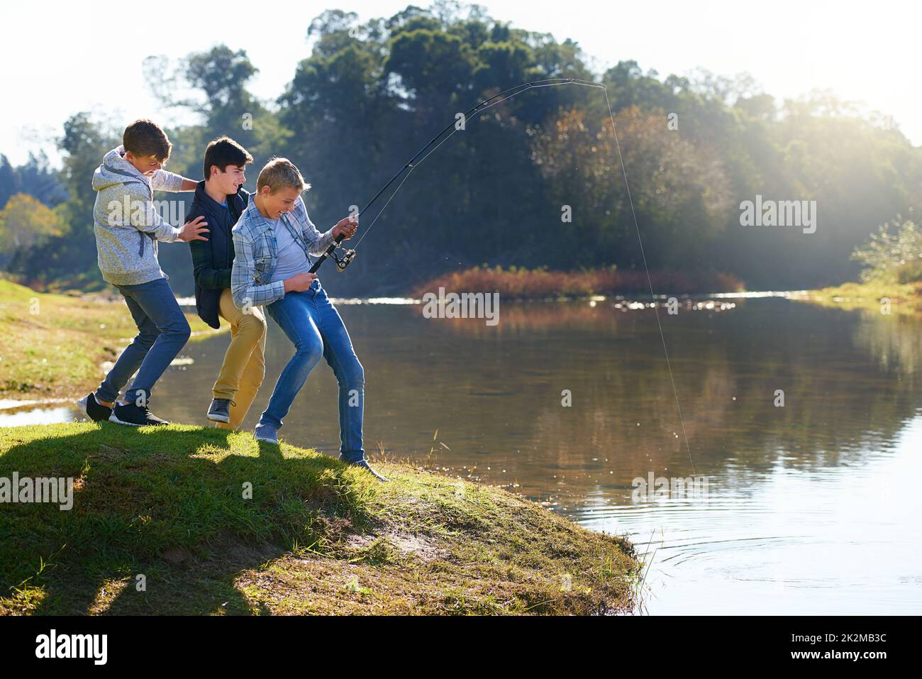 Its a big one. Shot of a group of young boys fishing by a lake. Stock Photo
