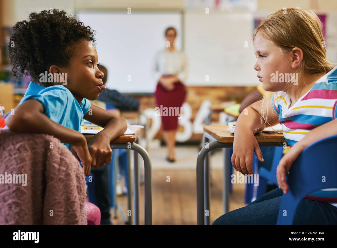 Bullying must be closely monitored. Shot of a young girl sitting in the classroom at school and pulling her tongue out at her classmate. Stock Photo