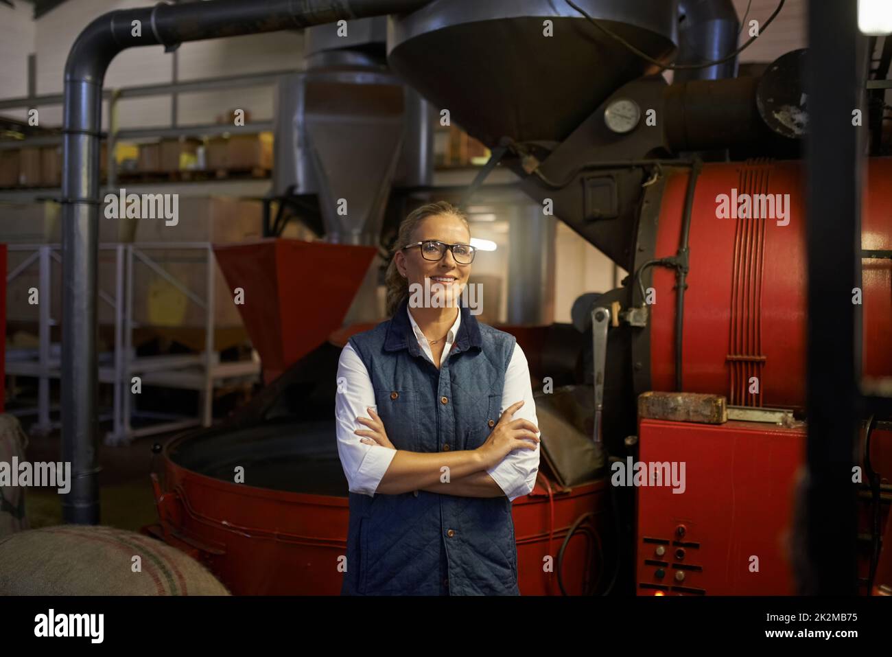 My whole day is a coffee break. Shot of an industrious entrepreneur posing in front of machinery in her coffee roastery. Stock Photo