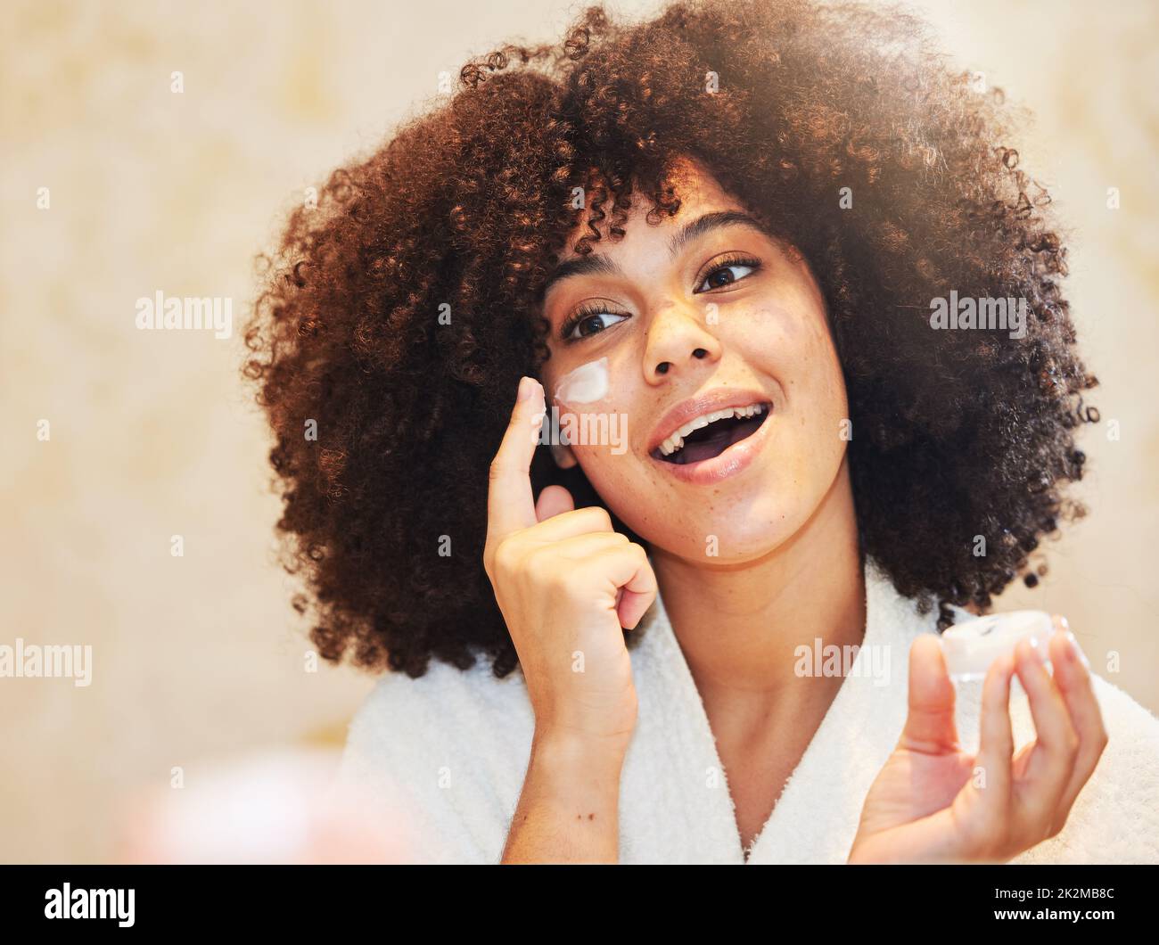 Keep your skin moisturised for the best results. Shot of a beautiful young woman applying moisturiser to her face. Stock Photo
