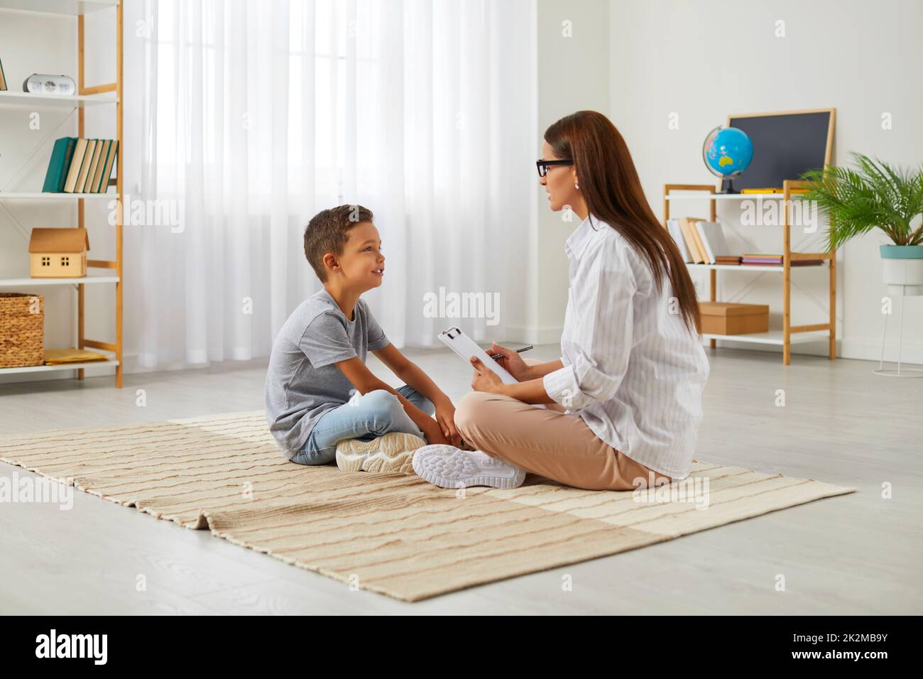 Female school counseling psychologist is talking to smart little boy during therapy session. Stock Photo
