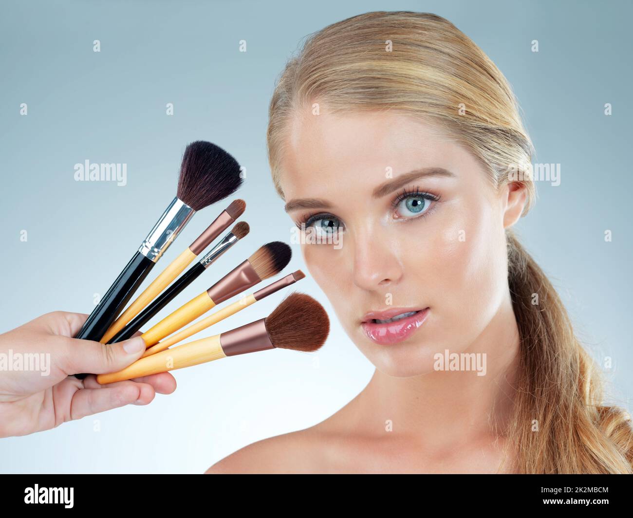Theres a brush for every occasion. Studio portrait of a beautiful young woman posing with makeup brushes against a blue background. Stock Photo