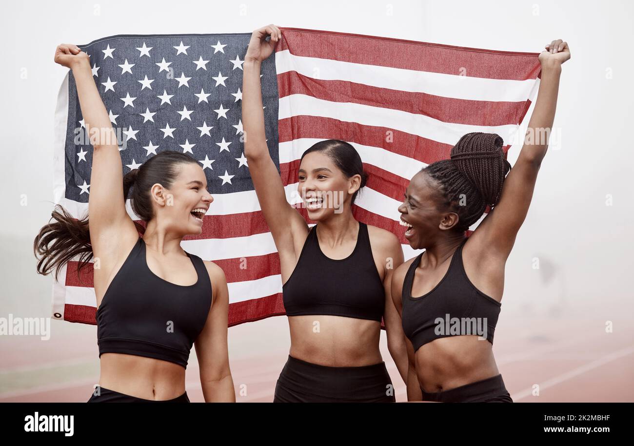 We finally did it. Shot of female athletes celebrating their win while holding a flag. Stock Photo